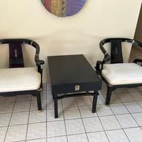 Two black armchairs and a matching table, with white cushions, in front of a wall with a circular art piece.