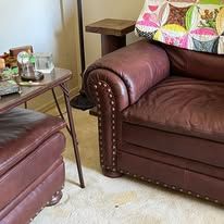 Brown leather couch with a matching ottoman and a small table with items on it.