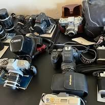A collection of cameras and accessories on a black surface, including cases and lenses.