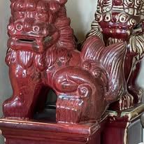 Two red, ornate Foo dog statues, one in front, on a wooden stand.