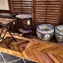 Wooden furniture, two small tables, a large ceramic pot, and a patterned wooden floor.