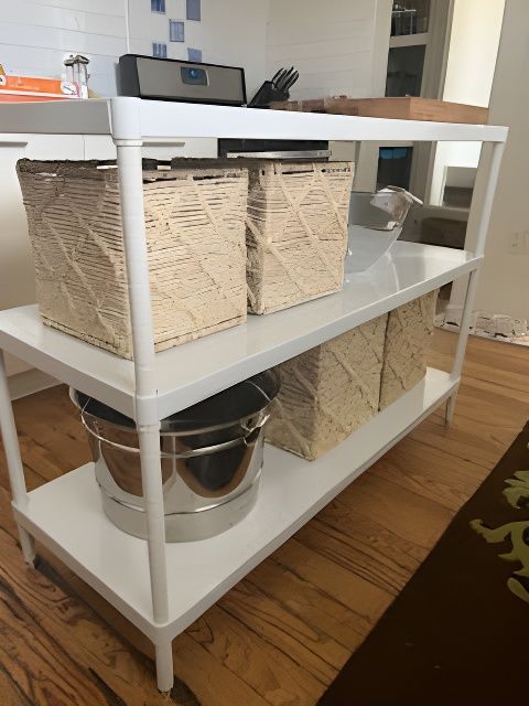 White shelving unit with woven baskets and stainless steel pot on wooden floor.