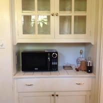 A built-in kitchen cabinet with a microwave oven inside, white, with glass-paneled doors.