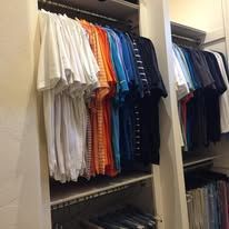 Clothes hanging in a closet, including white, orange, and blue shirts.