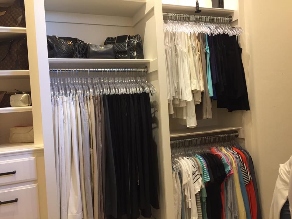 Walk-in closet with organized clothing on hangers, handbags on a shelf, and white cabinets.
