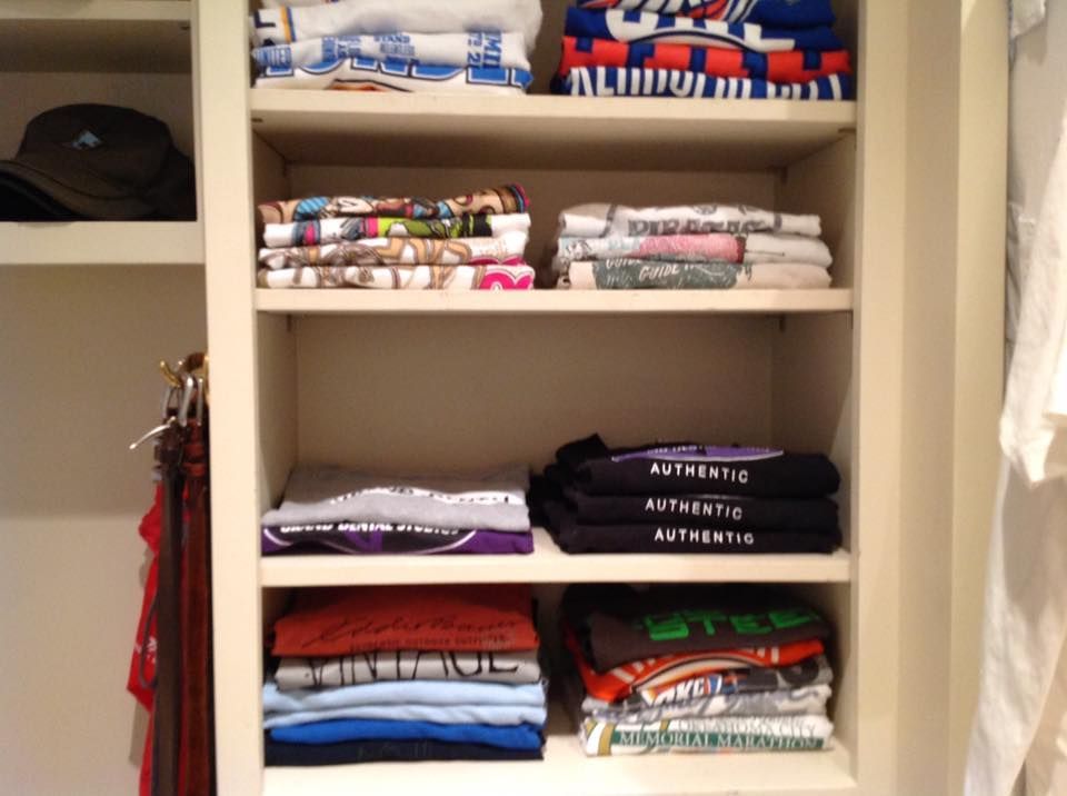 Shelves filled with neatly folded t-shirts in various colors. A hat is visible on the left shelf.