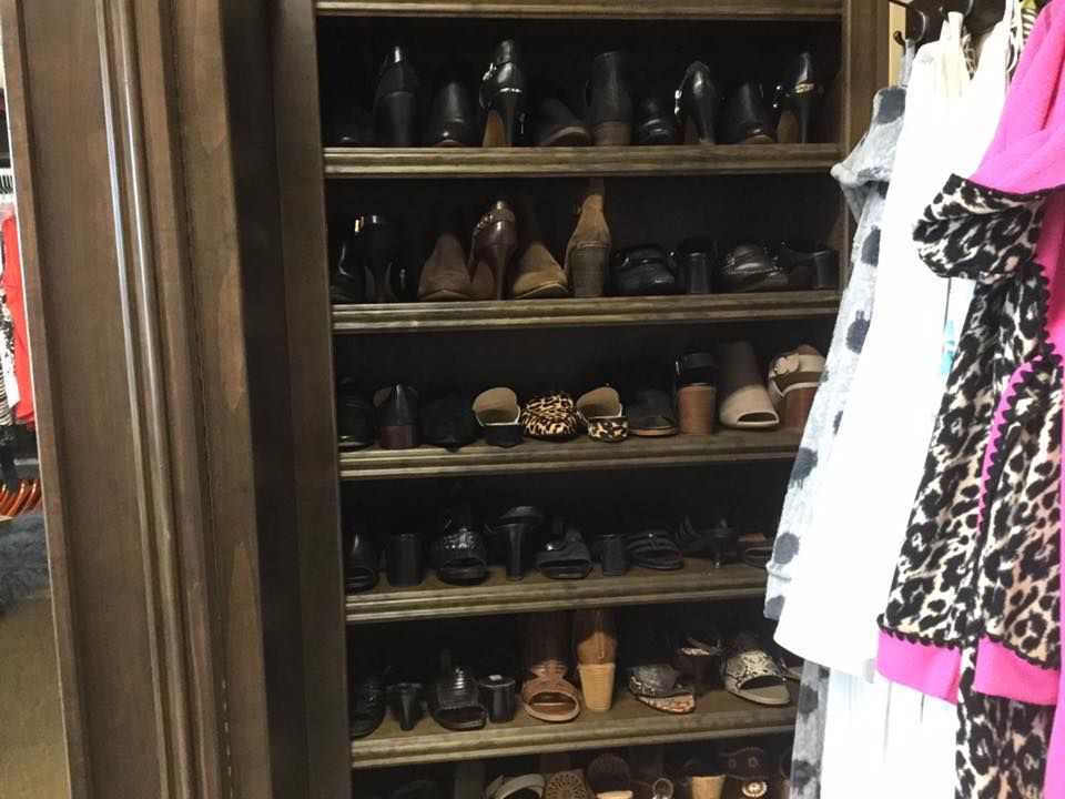 Wooden shoe rack filled with various women's shoes. Dresses hang to the right.