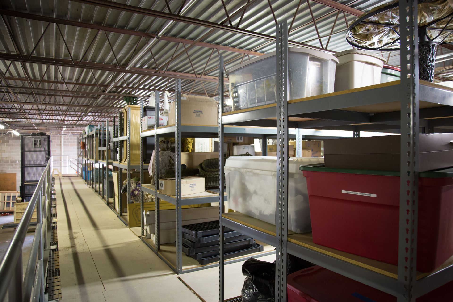 Shelves filled with boxes and containers in a storage room under a corrugated metal ceiling.