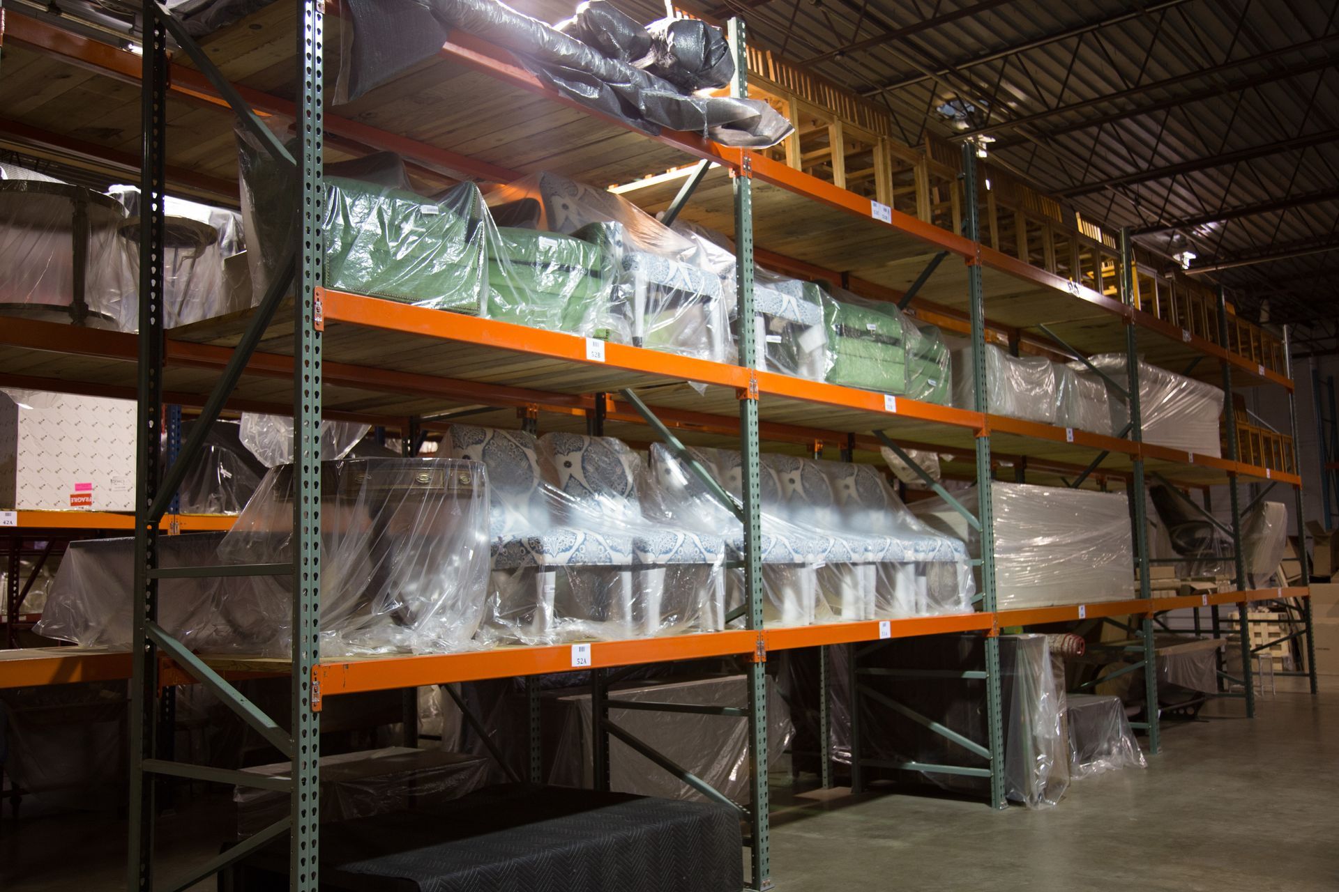 Shelves in a warehouse filled with wrapped machinery and equipment, lit by overhead lights.