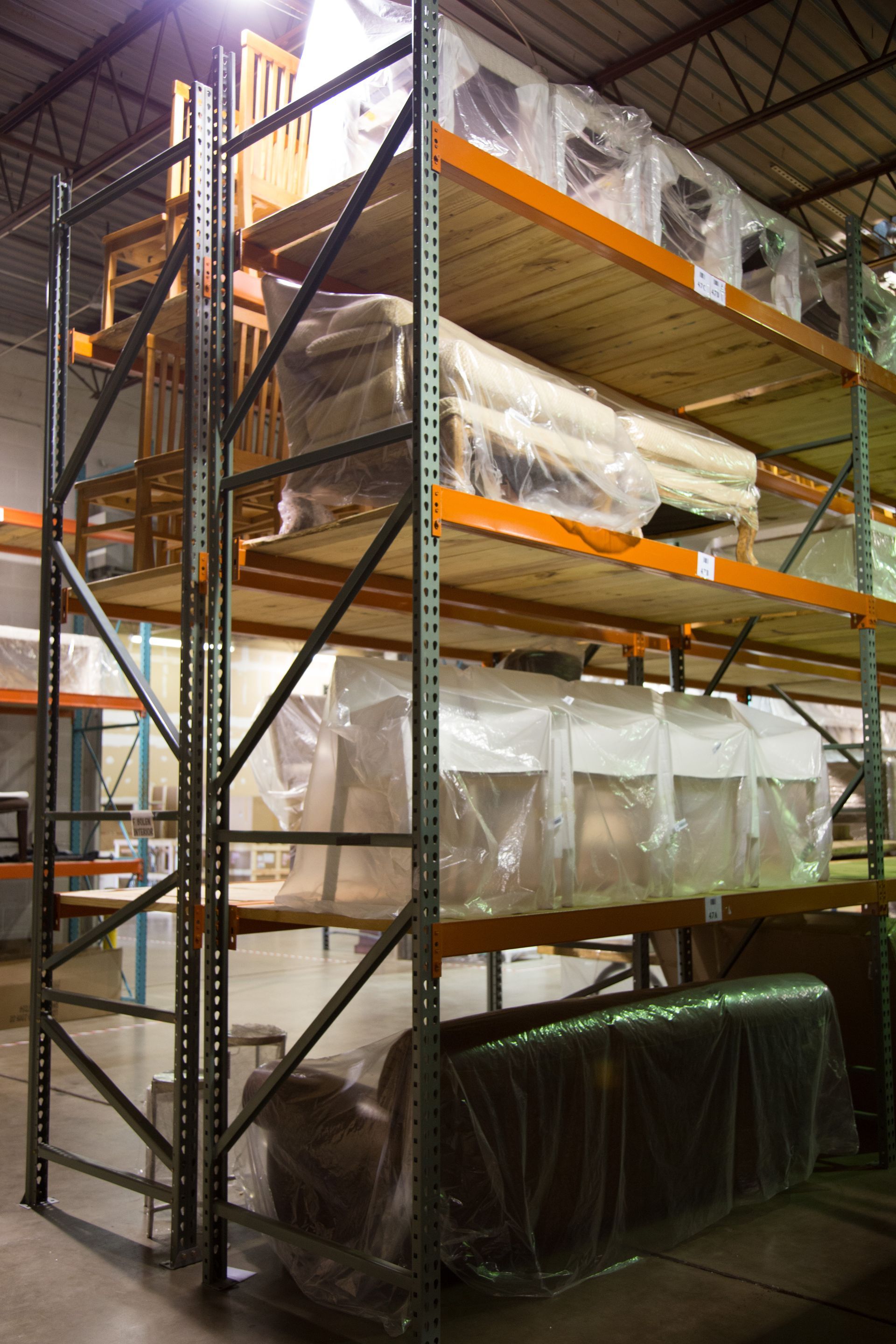 Metal shelving unit in a warehouse, loaded with wrapped furniture and boxes.