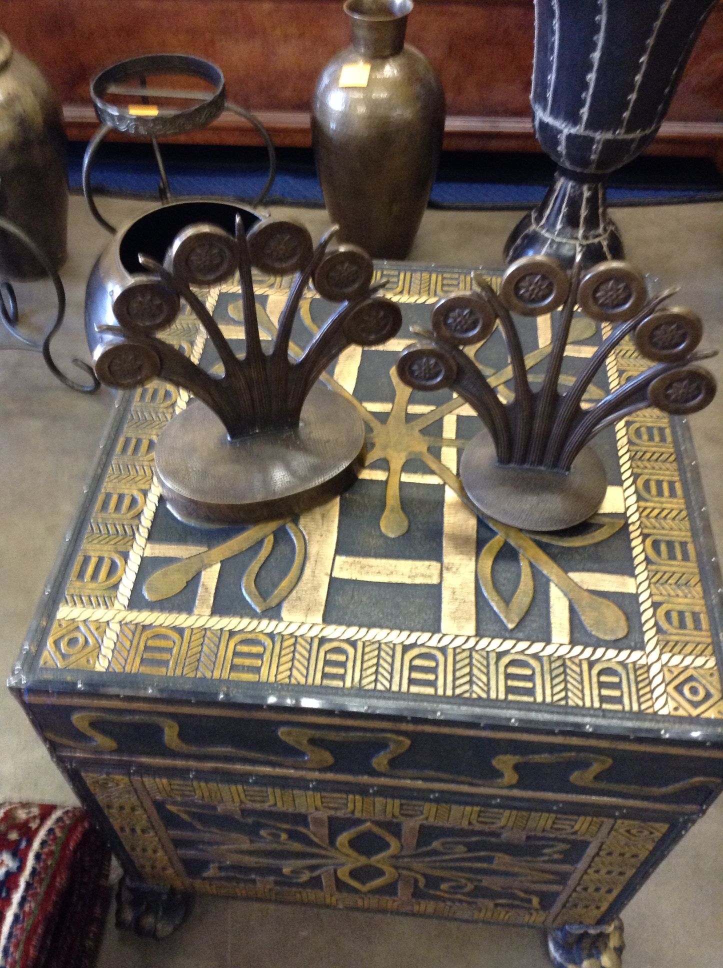 Two bronze decorative items on a black and gold patterned chest, with other decor visible in the background.
