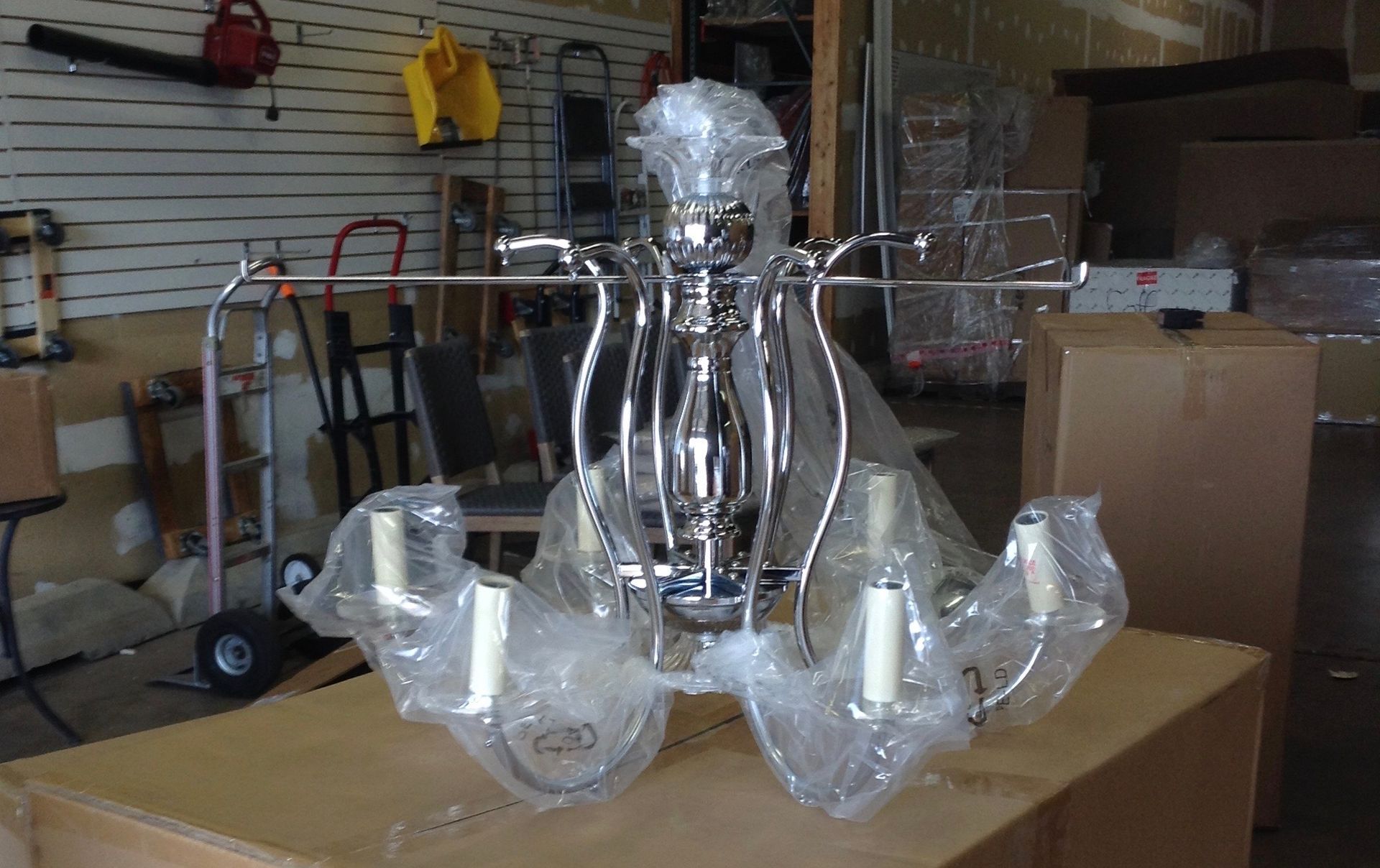 A chrome chandelier wrapped in plastic, sitting on a cardboard box in a storage space.
