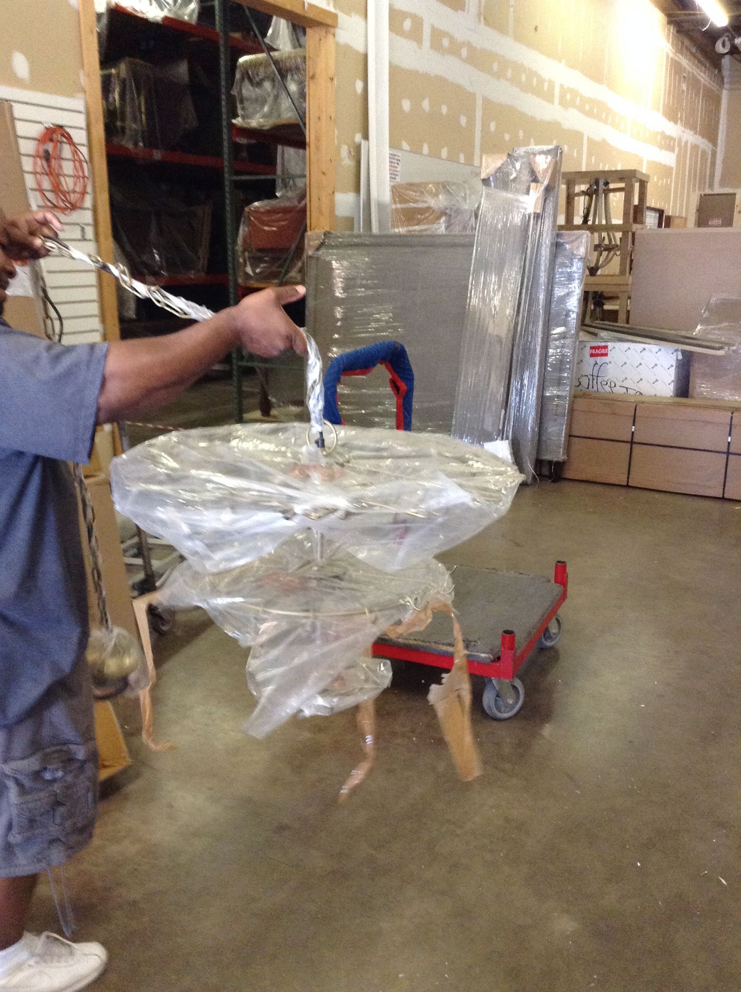 Man holding a chandelier wrapped in plastic, in a warehouse.