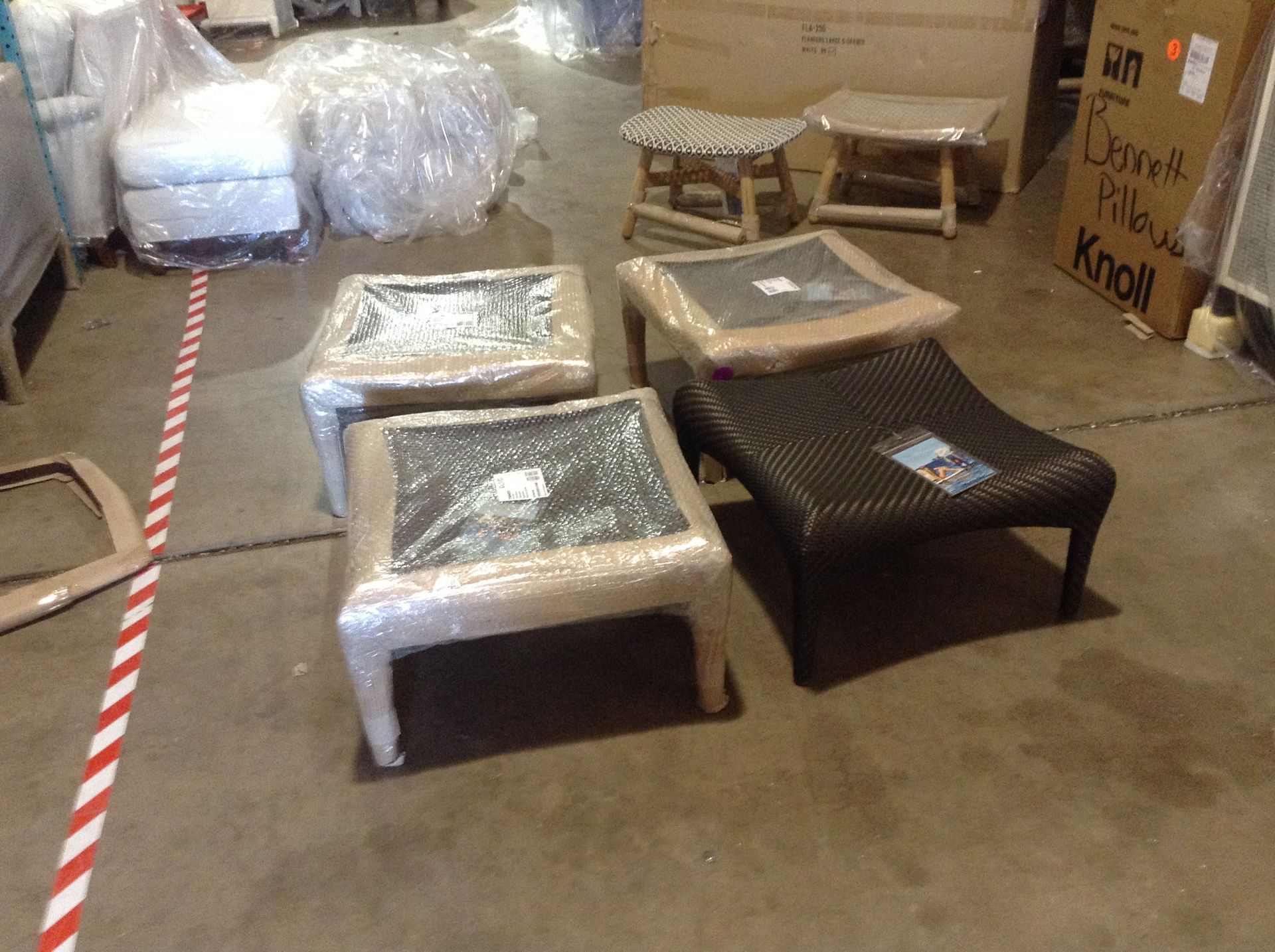 Four wrapped square ottomans and two small wooden stools in a warehouse.