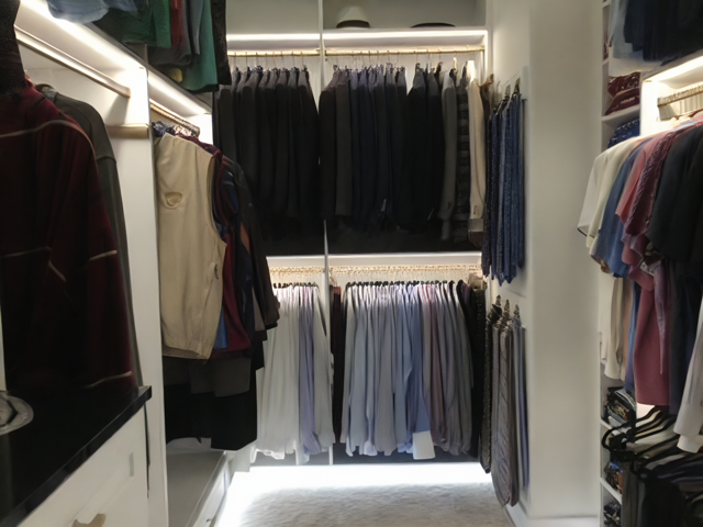 A walk-in closet with clothes hanging on rods; shades of black, blue, and neutral colors.