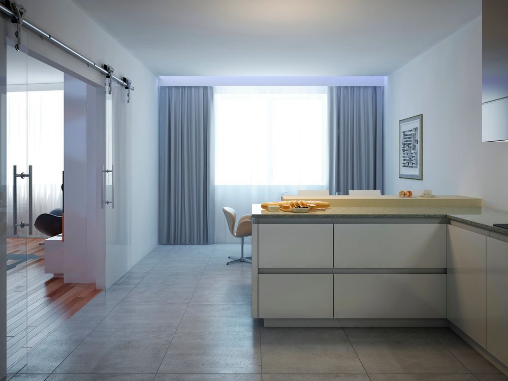 Cucina moderna con mobili bianchi, isola e ampia finestra con tende. Porta scorrevole in vetro a sinistra.