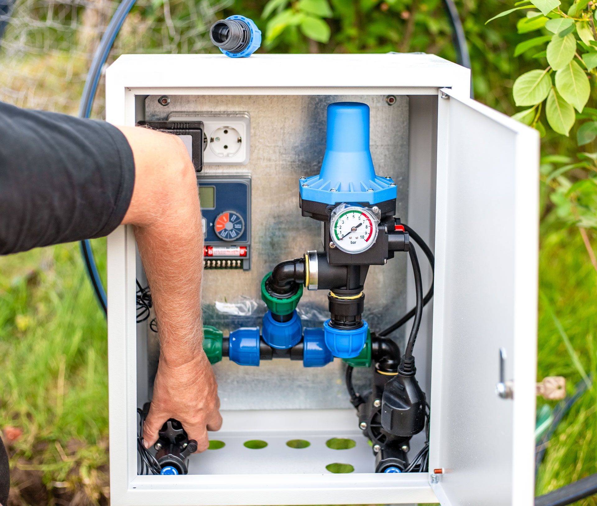 Hand adjusting a blue water filter system inside an open outdoor control cabinet