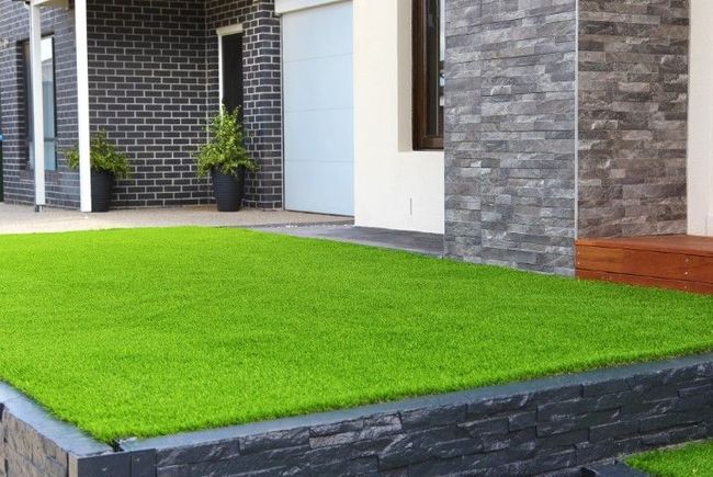 A path of artificial grass on the front yard of a brick home with white paint. 