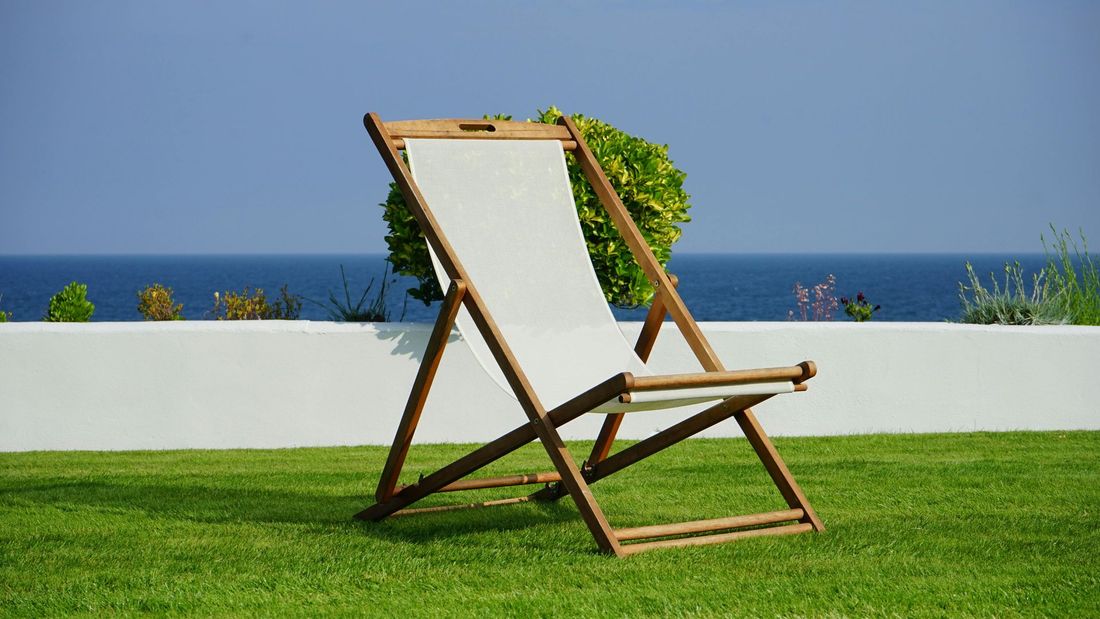 White lawn chair on astro turf in a backyard withi an ocean in the background. 