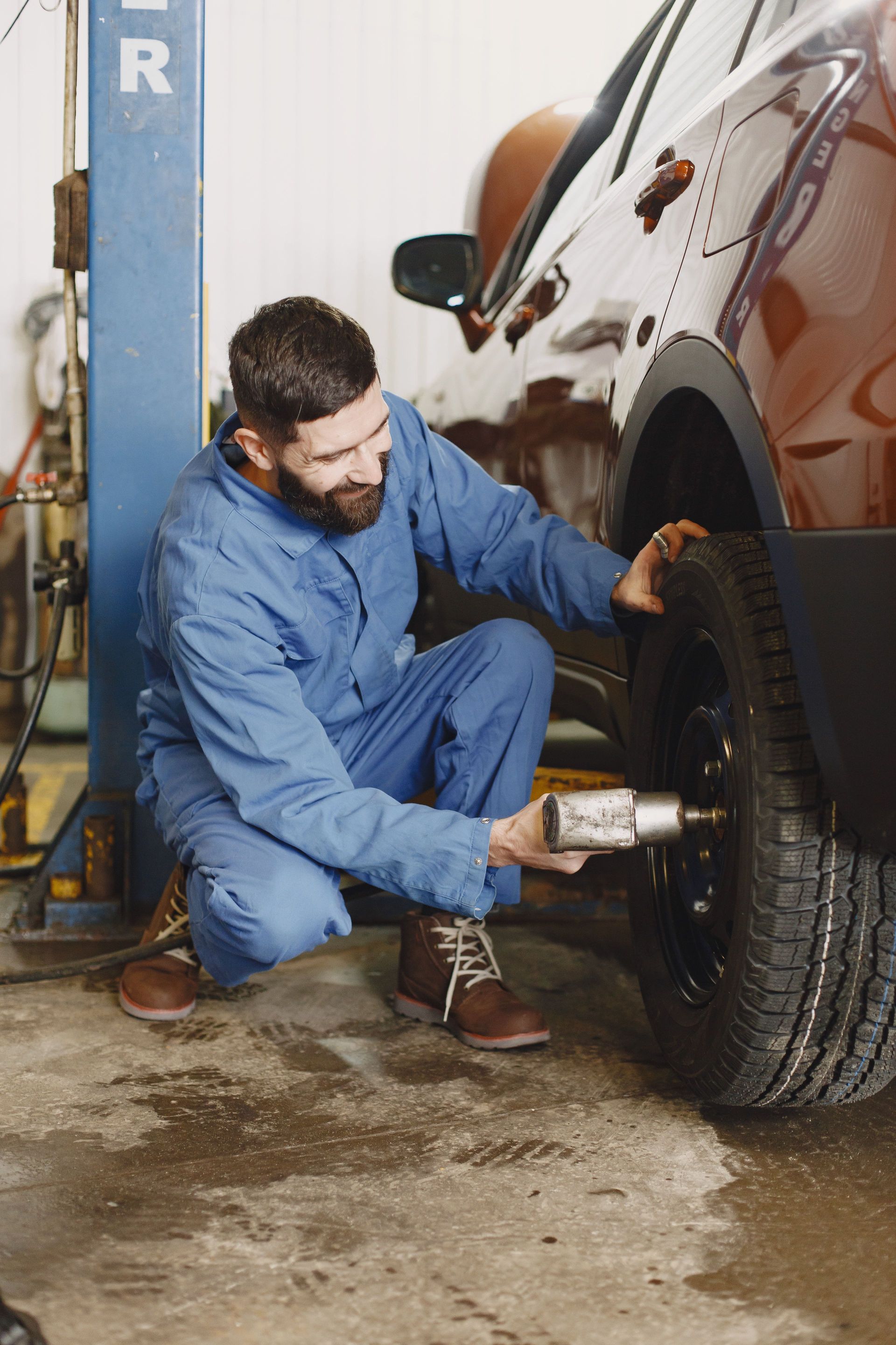 Mechanic in blue coveralls tightening a car wheel in a garage