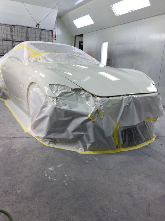 White car wrapped in protective plastic and masking tape inside a paint booth