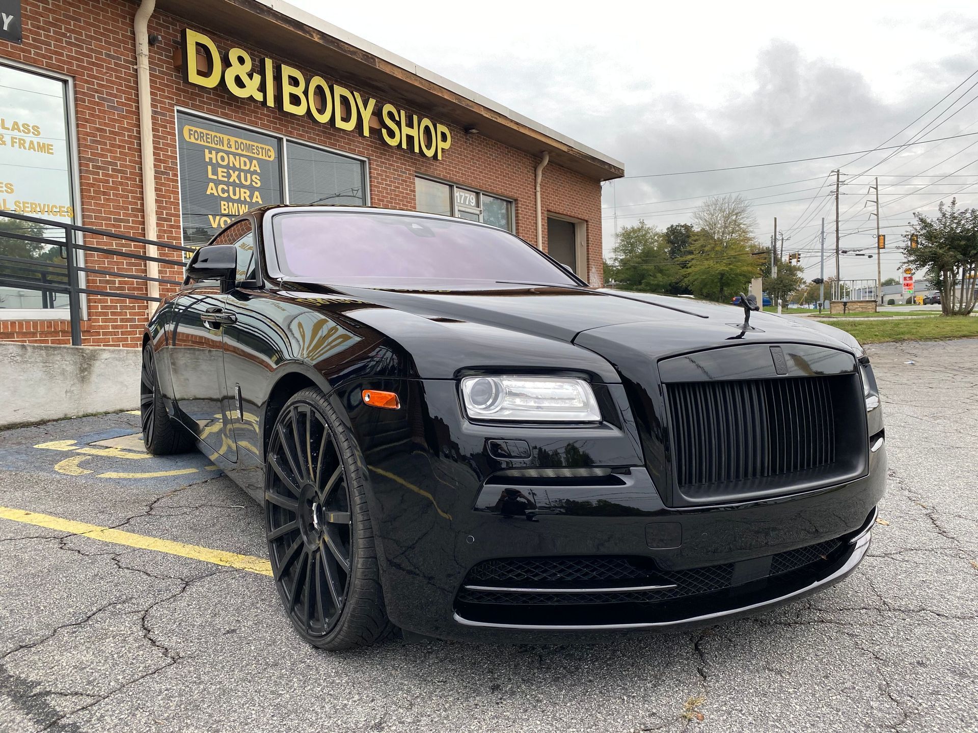 Black luxury sedan parked outside a body shop on a cloudy day