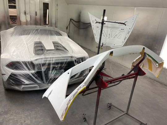 Black car in a paint booth, front covered with masking plastic and tape for repainting