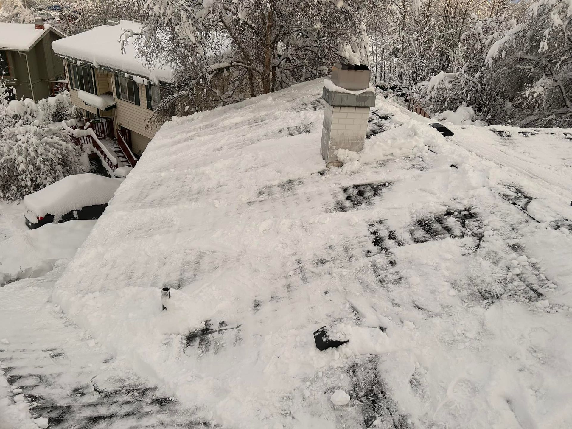 Snow-covered roof of a house with a chimney and snowy surroundings.