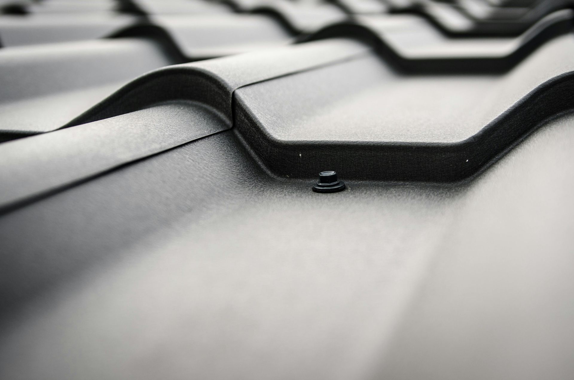 Close-up of a black metal roof with overlapping curved panels and a single visible fastener.