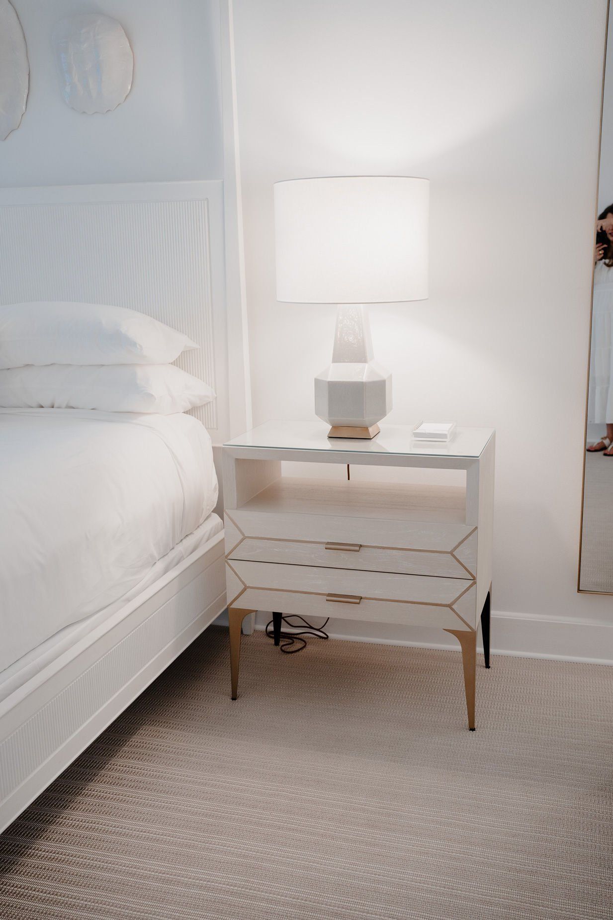 A bedroom with a bed , nightstand , lamp and mirror.