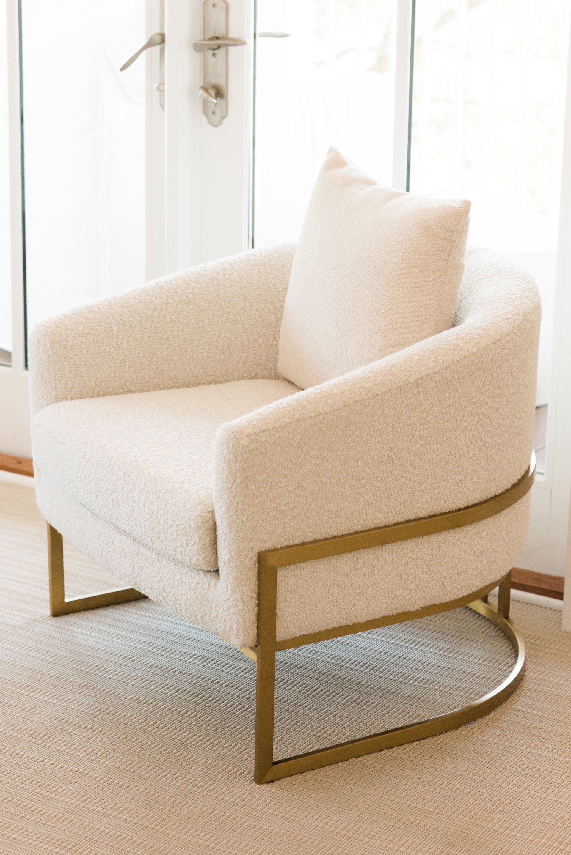 A white chair with a gold frame is sitting on a rug in front of a window.