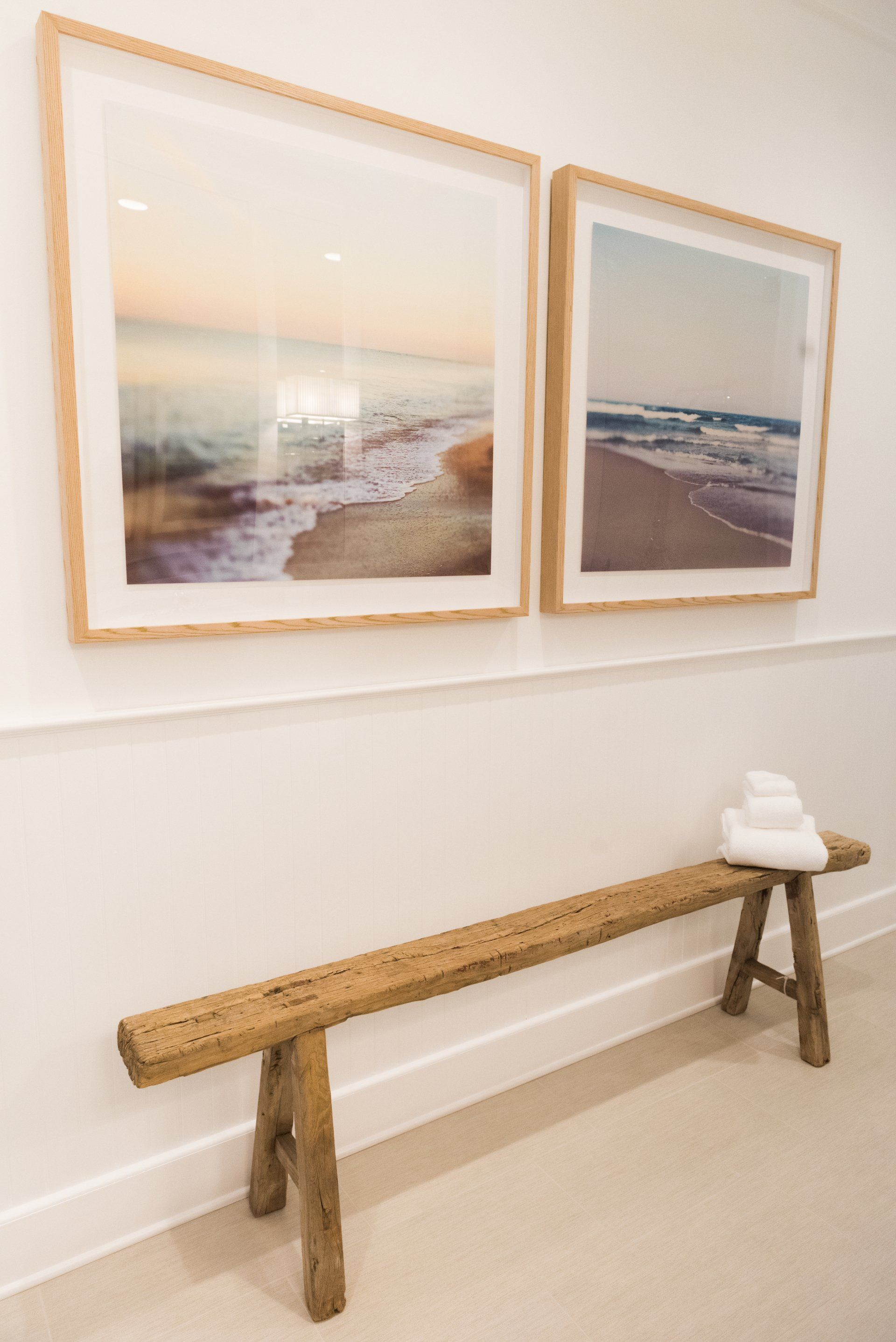 A wooden bench in a hallway with two framed pictures on the wall above it