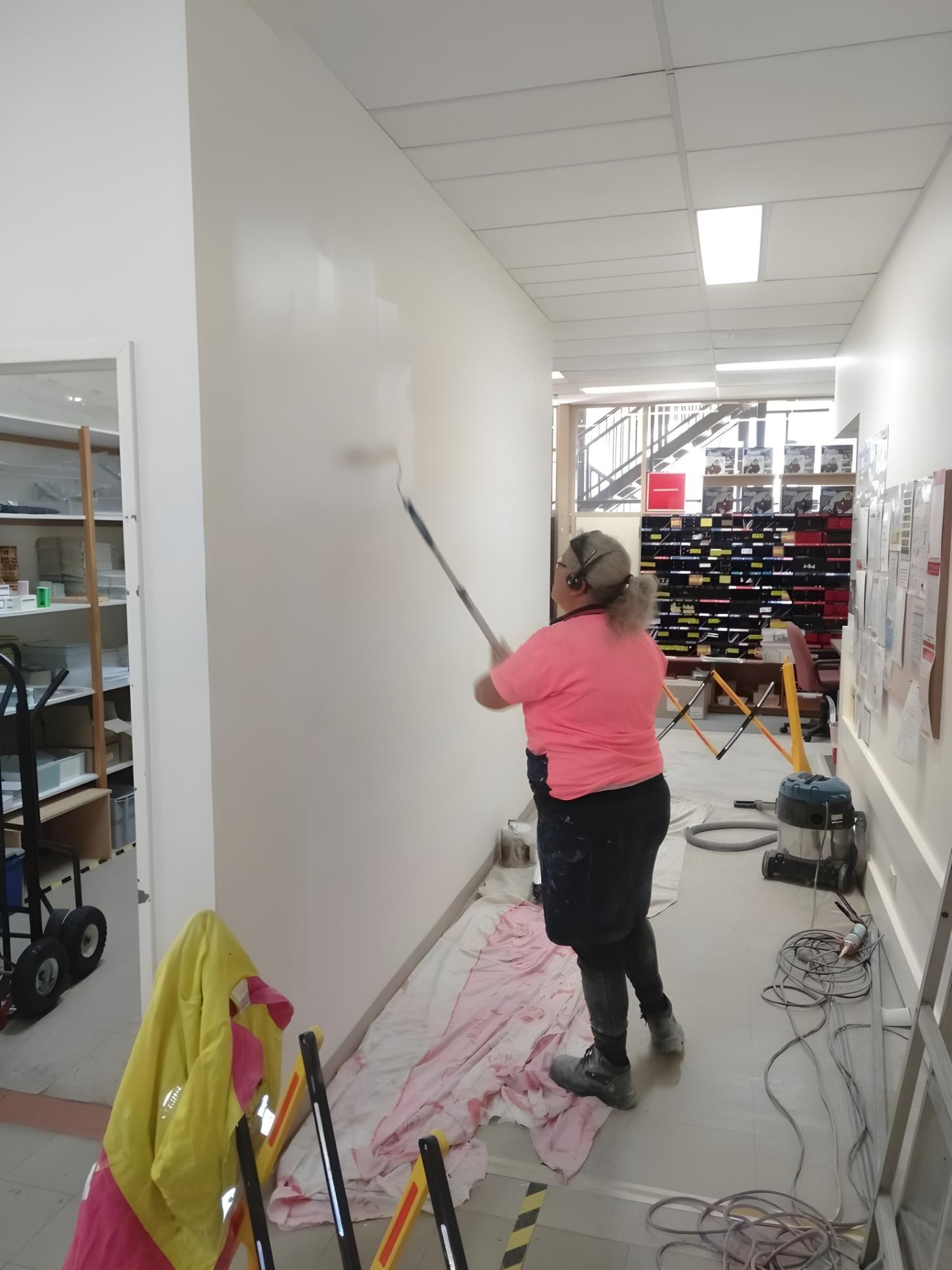 A Woman in a Pink Shirt is Painting a Wall With a Roller  — Handyman Bundaberg In Burnett Heads, QLD