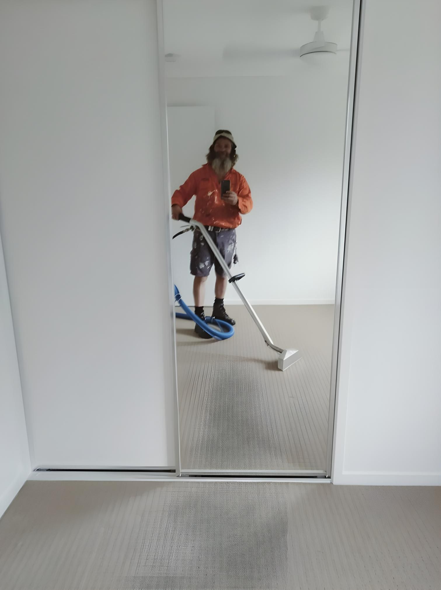A Man is Cleaning a Carpet With a Vacuum Cleaner in Front of a Mirror — Handyman Bundaberg In Burnett Heads, QLD