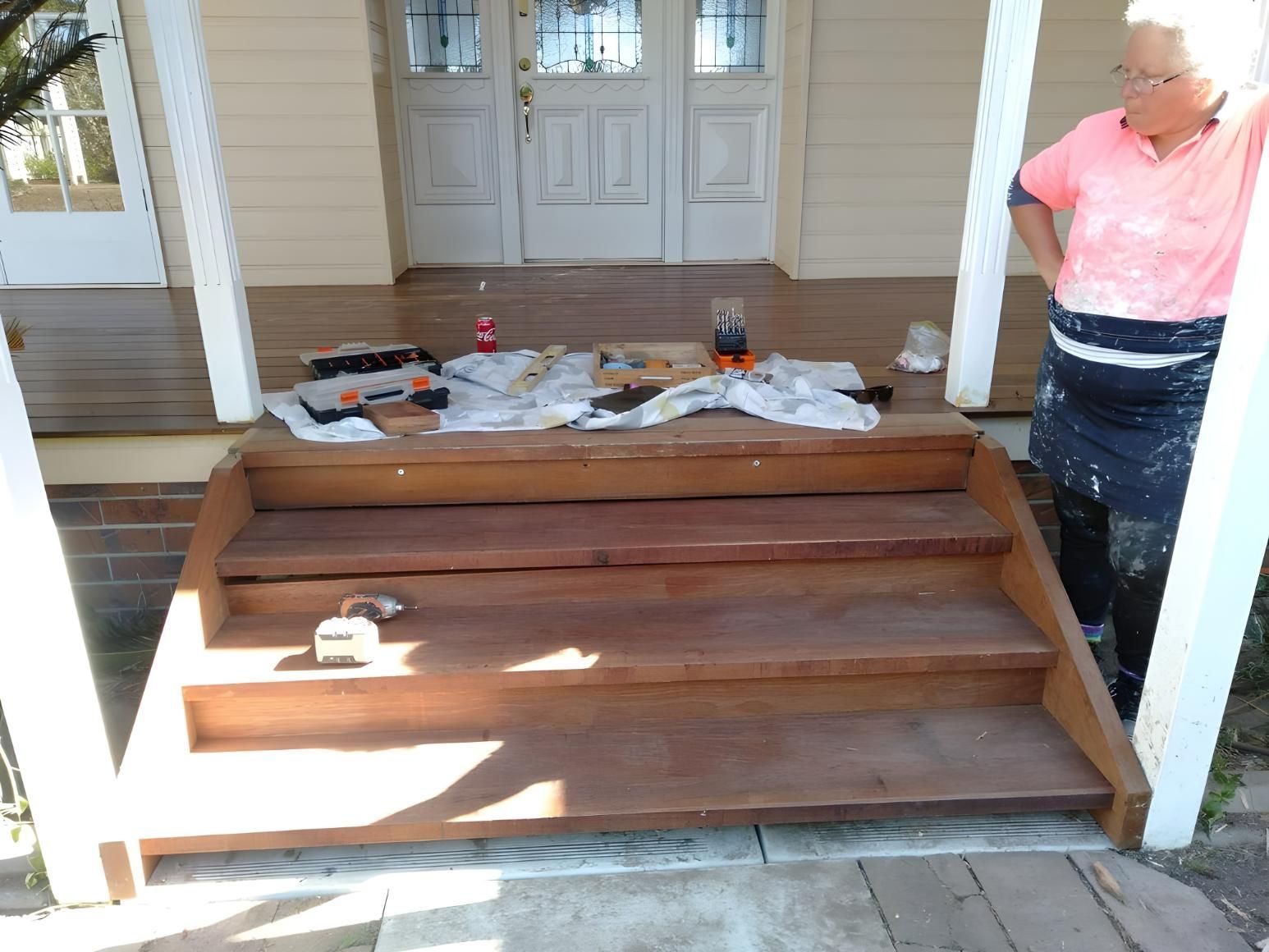 A Man is Standing on a Porch Next to a Set of Wooden Stairs — Handyman Bundaberg In Burnett Heads, QLD