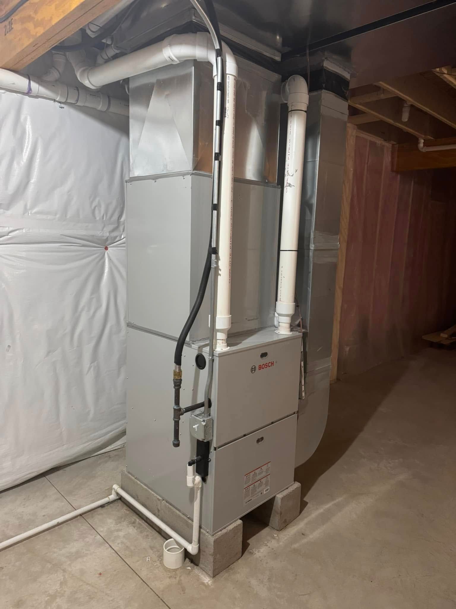 A gas furnace is sitting in a basement next to a wall.