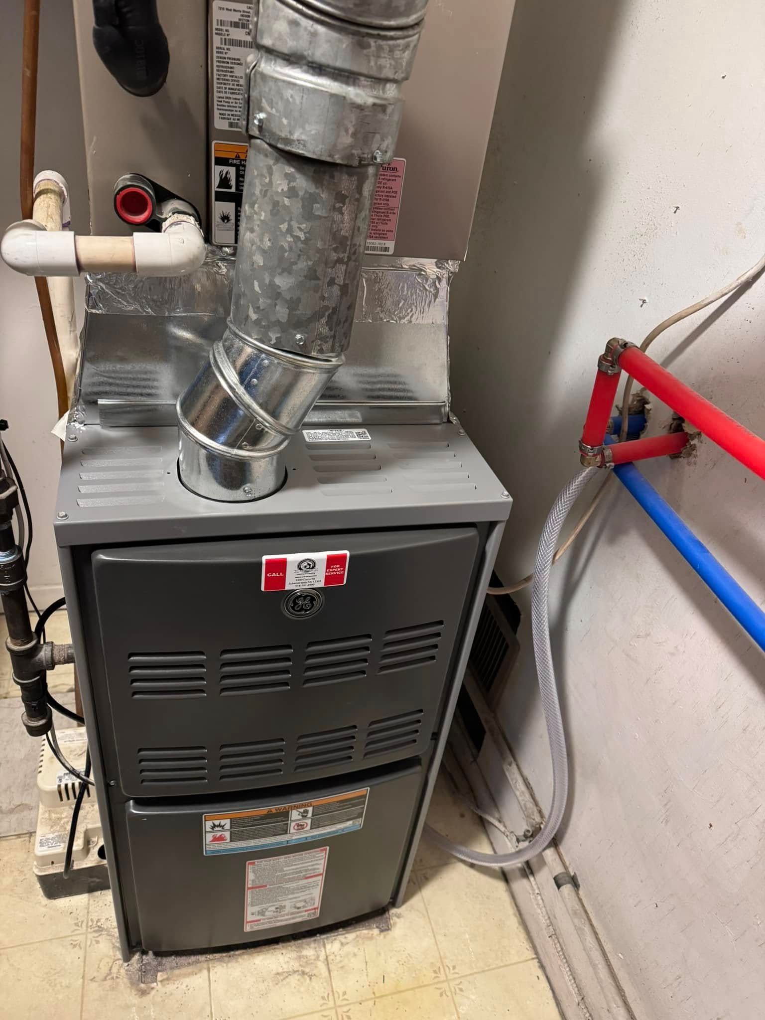 A furnace is sitting in a room next to pipes.