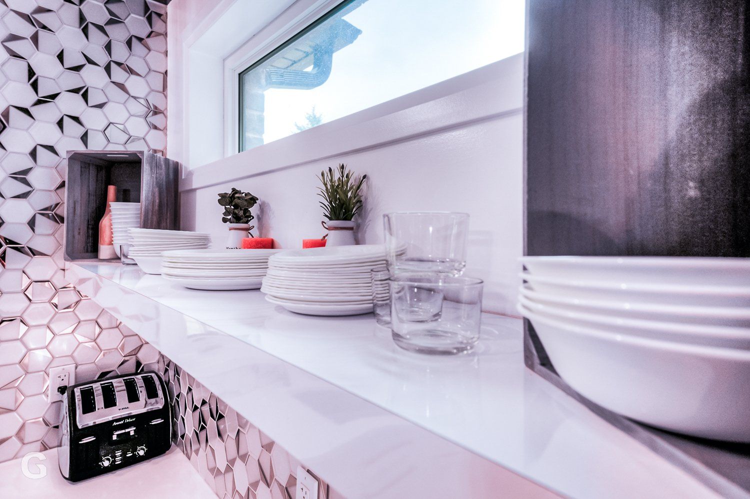 A kitchen shelf with plates , bowls , glasses and a toaster oven.