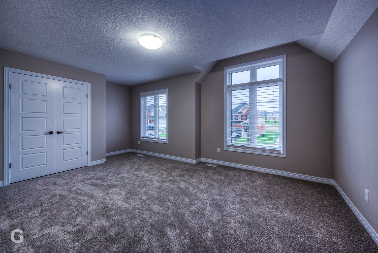 An empty bedroom with a carpeted floor and two windows.