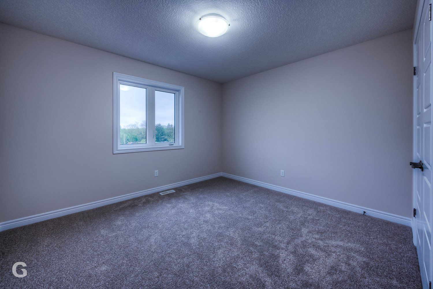 An empty bedroom with a window and a carpeted floor.