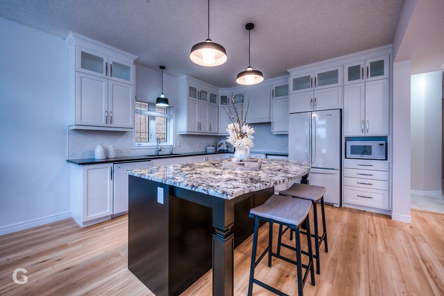 A kitchen with white cabinets , granite counter tops , stools and a large island.