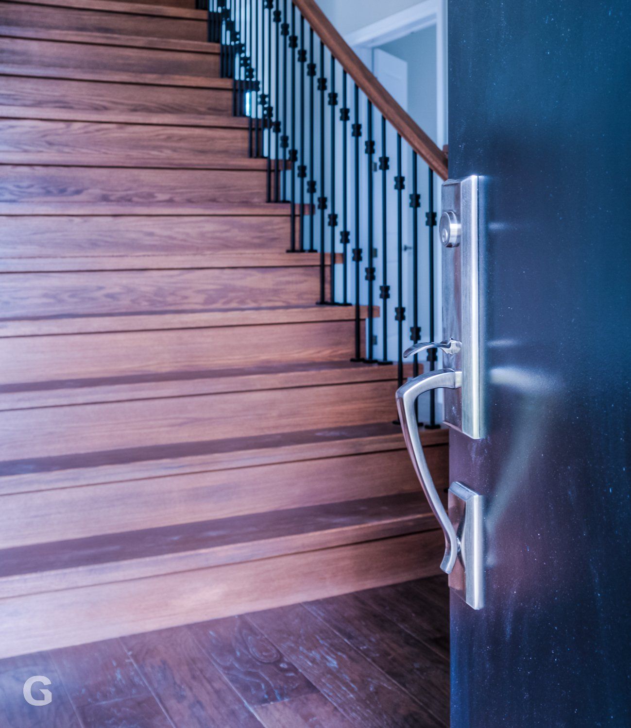 A wooden staircase with a metal railing and a black door
