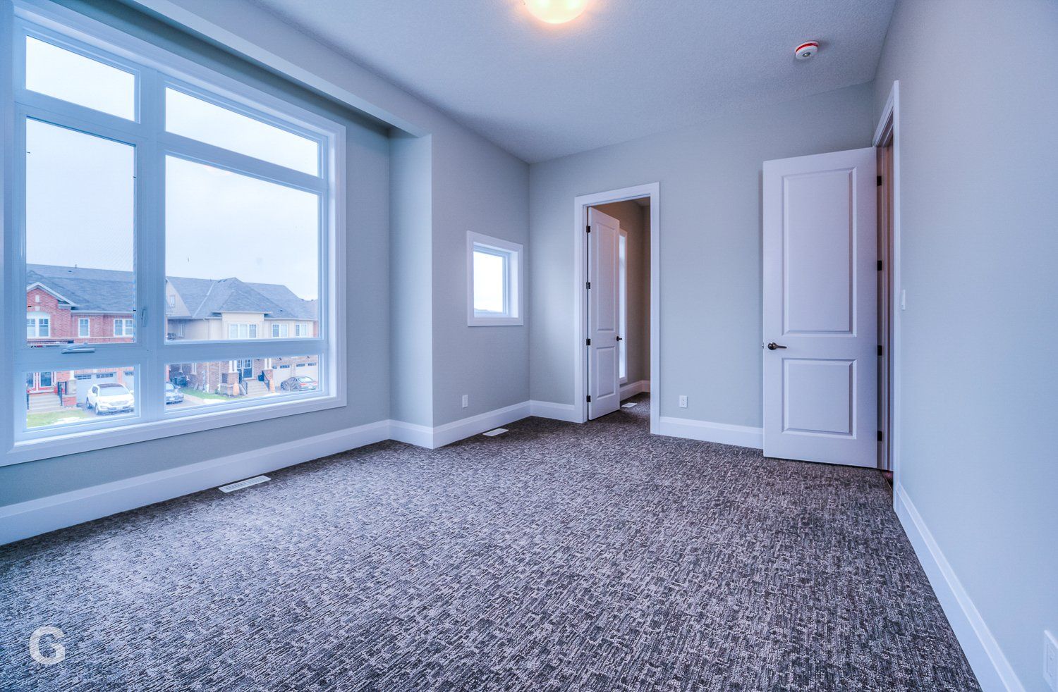 An empty bedroom with a large window and a carpeted floor.