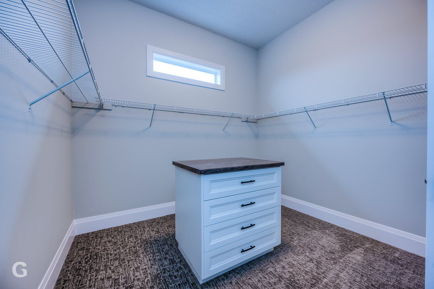 A walk in closet with a dresser and a window.