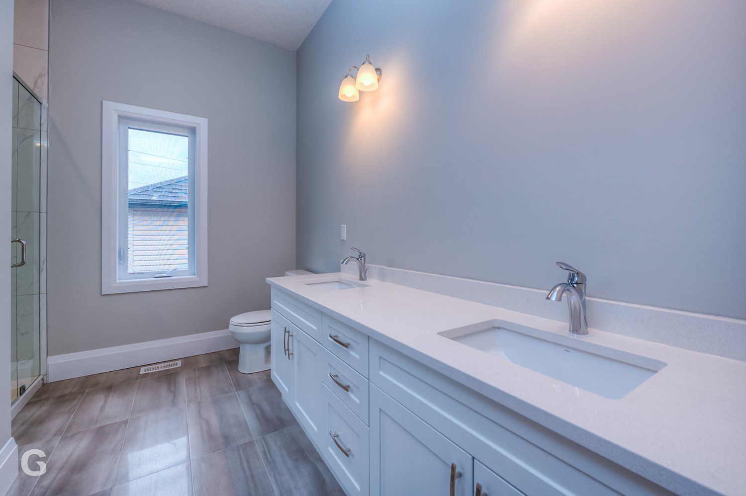 A bathroom with two sinks , a toilet , and a window.