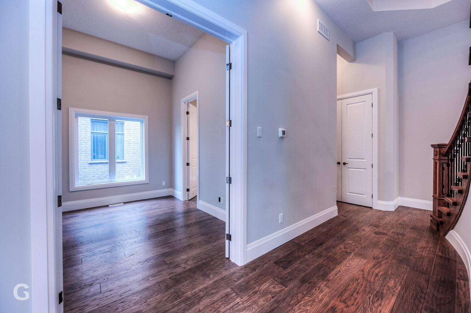 A hallway in a house with hardwood floors and a staircase.
