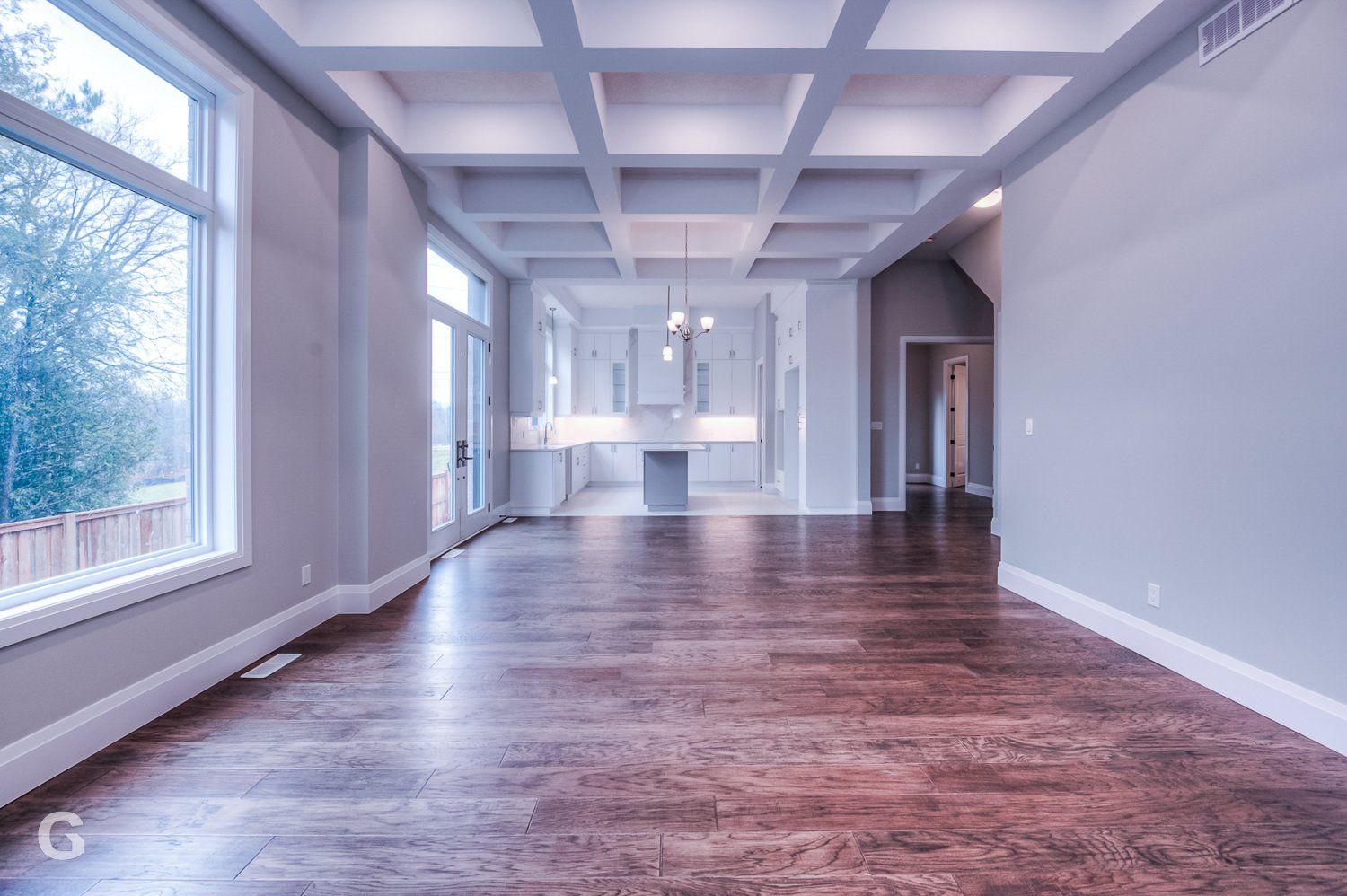 A large empty room with hardwood floors and a coffered ceiling.