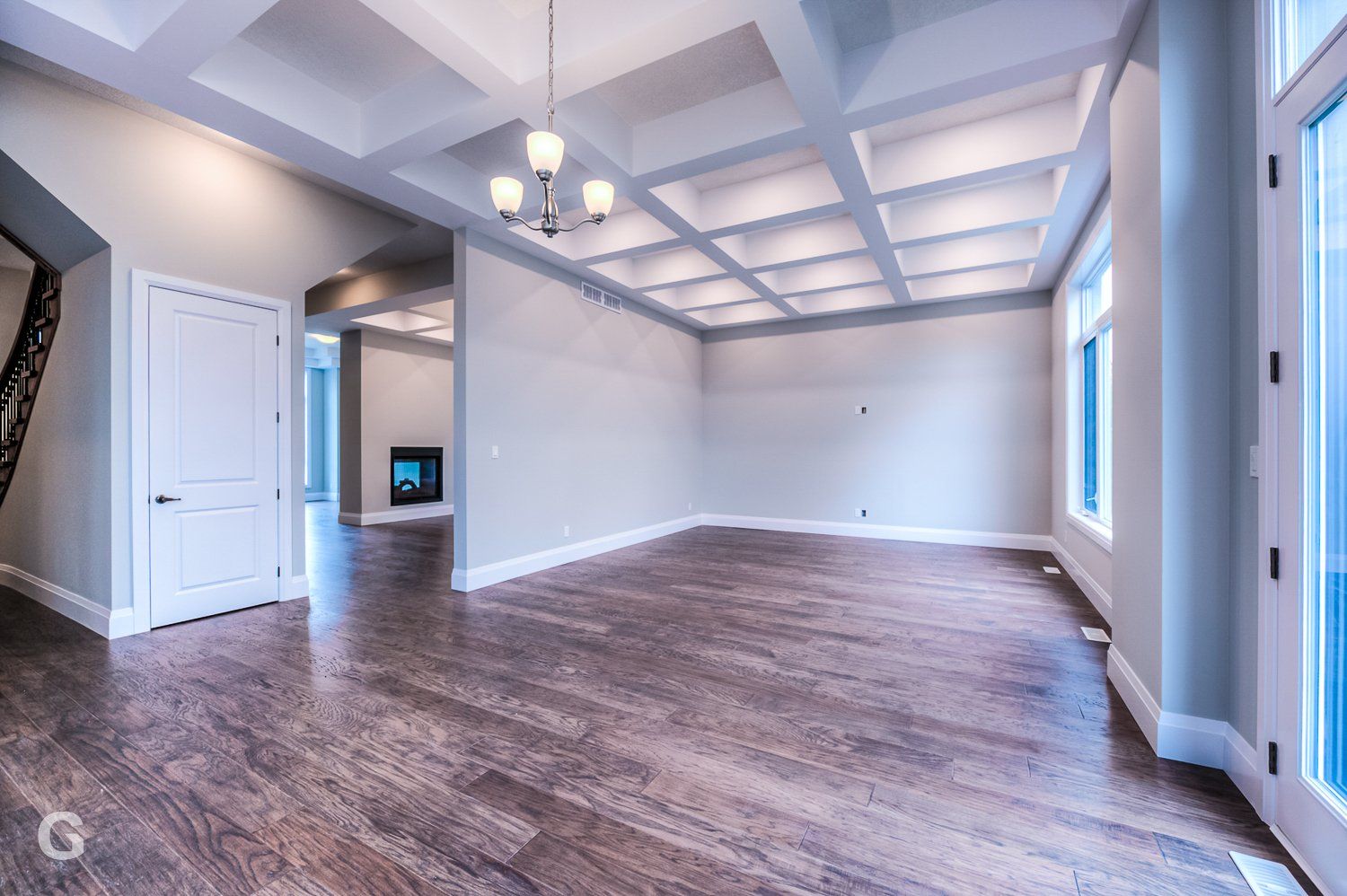 An empty living room with hardwood floors and a chandelier hanging from the ceiling.