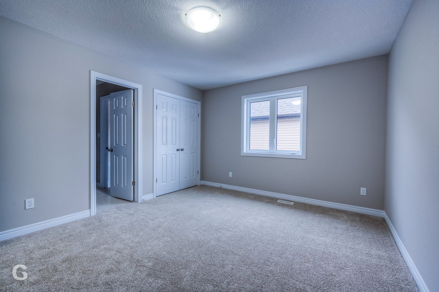 An empty bedroom with a carpeted floor and a window.
