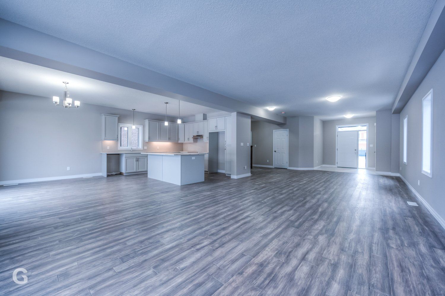 A large empty room with hardwood floors and a kitchen.